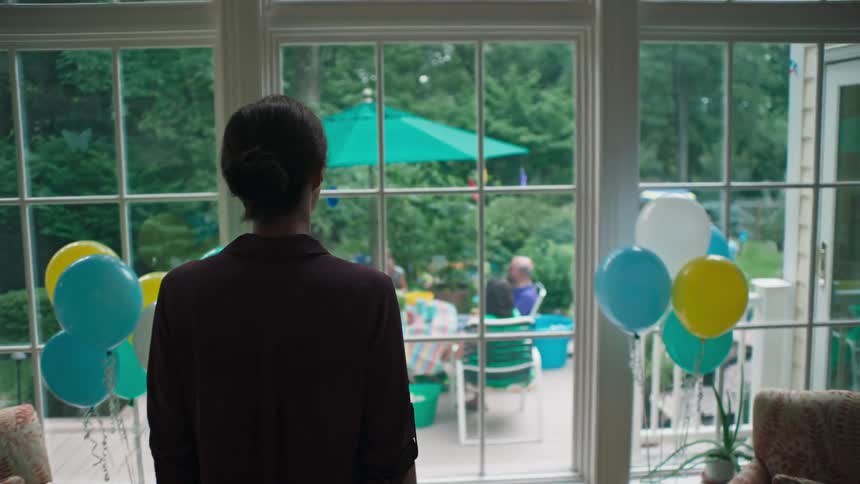 Woman walks towards windows to look over backyard party