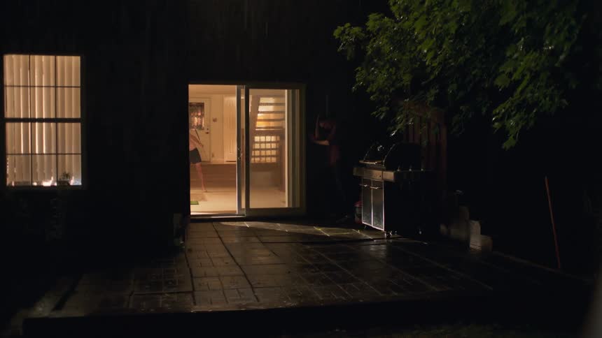 Man wearing shorts drives golf ball out through sliding glass doors into rain