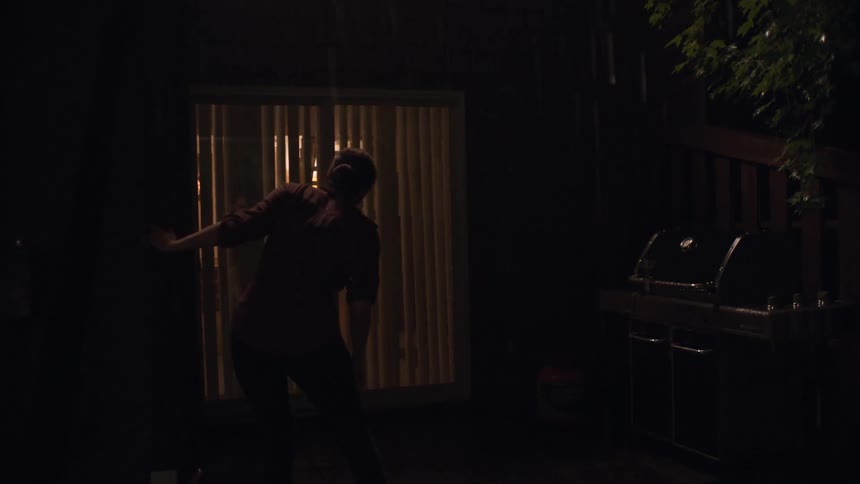 A woman sneaking through the backyard of a house on a rainy night