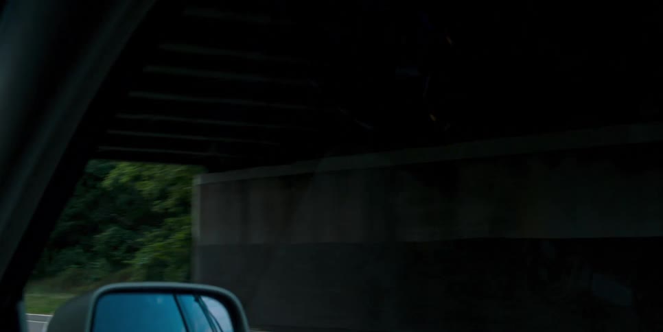 A vehicle drives along a tree lined road and under a bridge