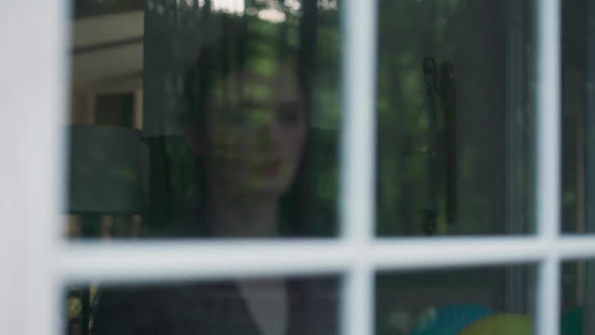 A woman stands at her back door and looks out the window