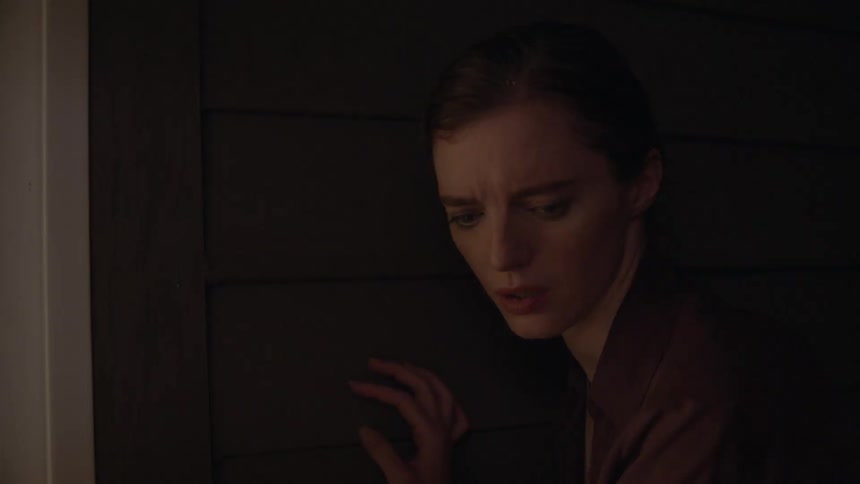 A woman touches and listens at the door then looks nervously and anxiously away