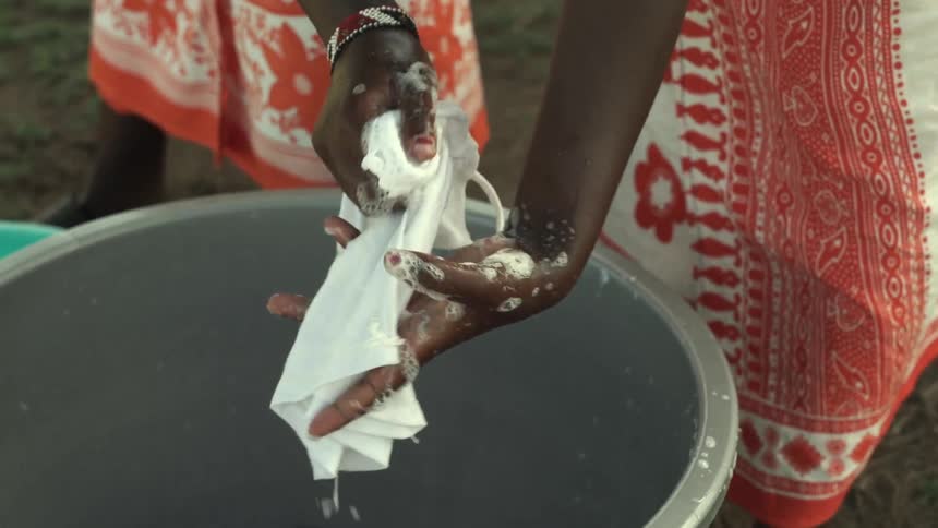 Women wash clothing in buckets outdoors in the daytime