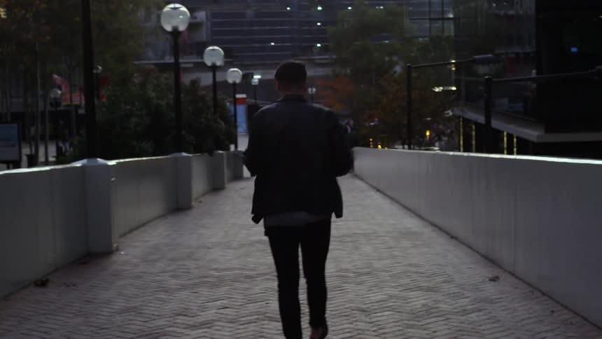 A man is walking down a sidewalk towards some buildings at sunset