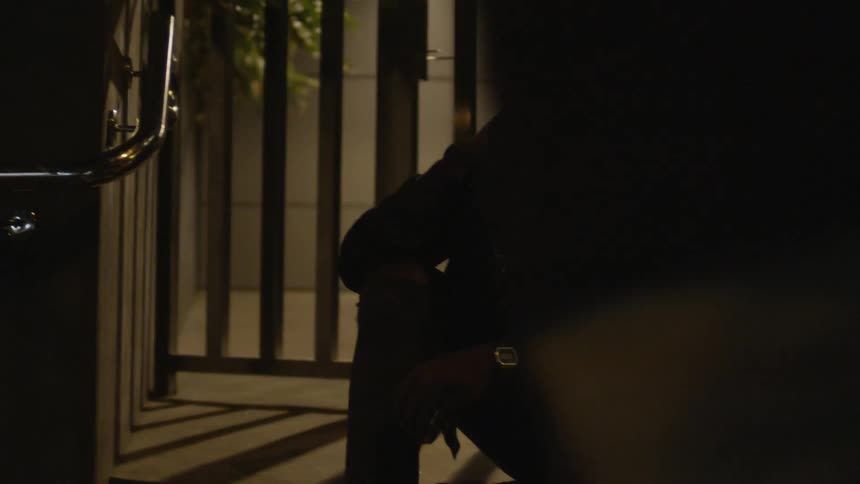 Man sitting outside at night hanging his head sadly while people walk by