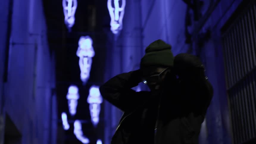 A man in distress clasps his hands behind his head in an urban alley at night