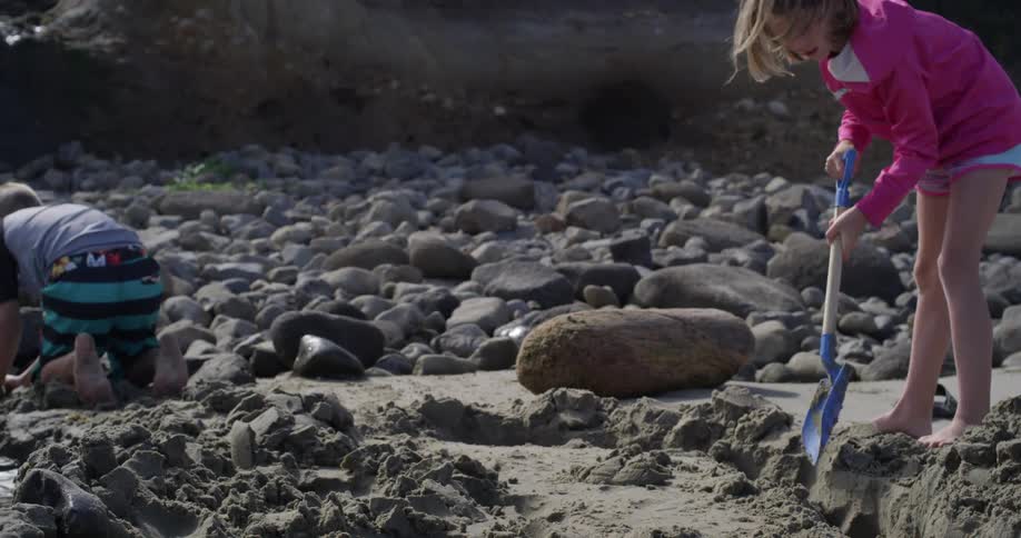 A girl digs with a shovel on a beach