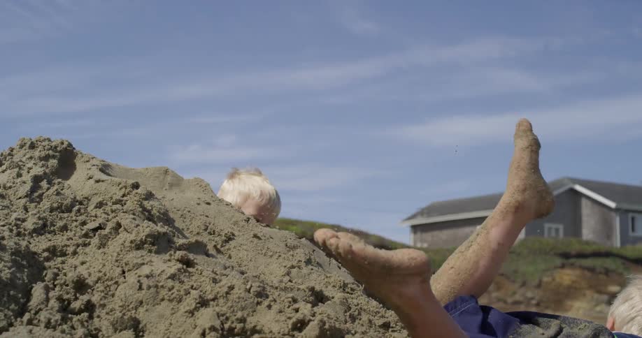 Two young boys playing in the sand on a beach in front of a house built on an embankment