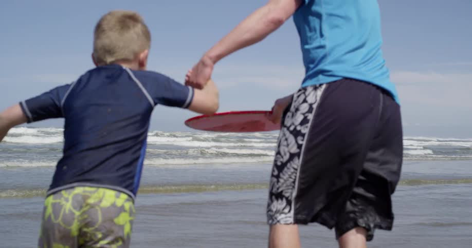 A man helping a little boy learn how to use a water disk before they both end up stumbling