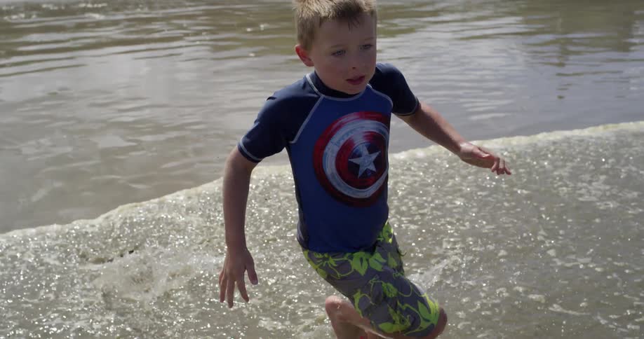 A man and a young boy play in the surf on a beach