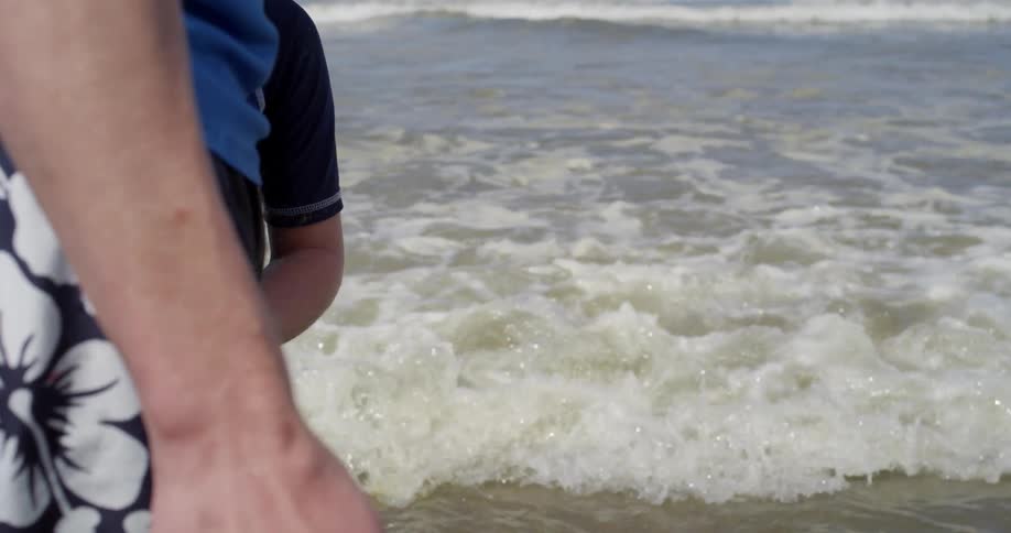 A child holds and adult's hand at the beach
