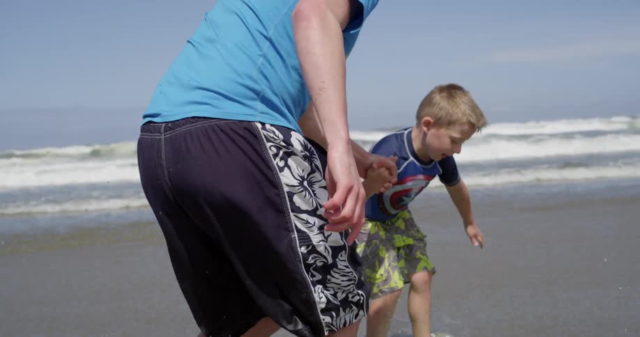 A man and boy run and slide on a beach