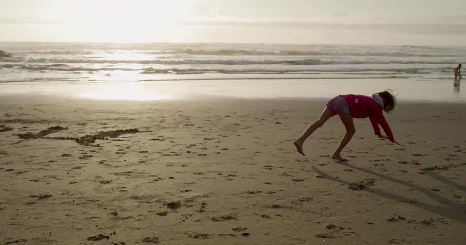 A girl does handstands and cartwheels on a sunny beach