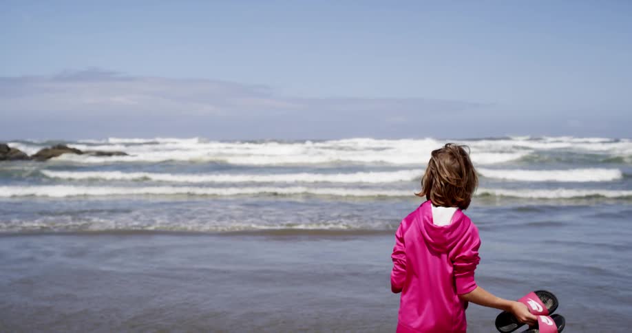 A woman jumps and waves while standing on the beach