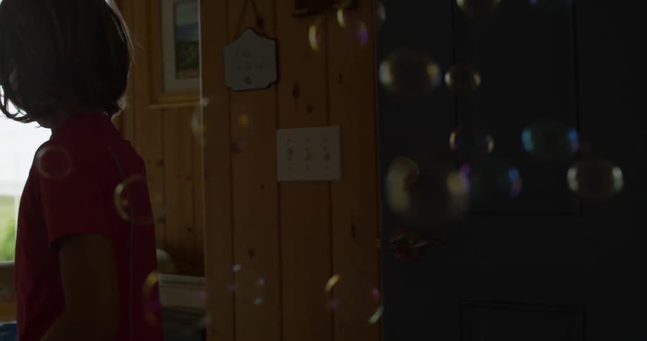 A young girl uses a bubble blower indoors