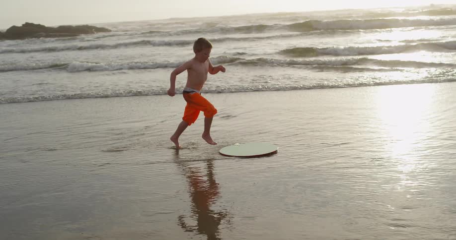 A boy is running on the beach sliding on a board