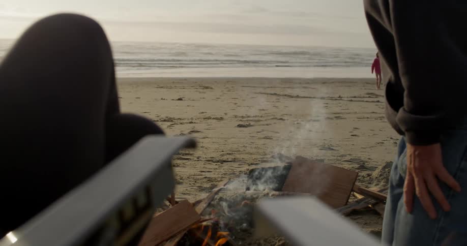 A person adds wood to a fire on a beach
