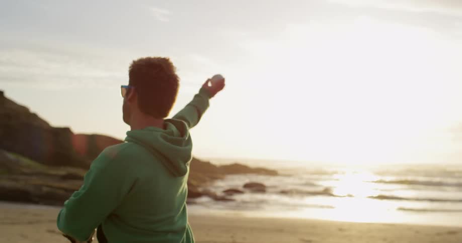 A man wearing a baseball glove and throwing a ball on the beach