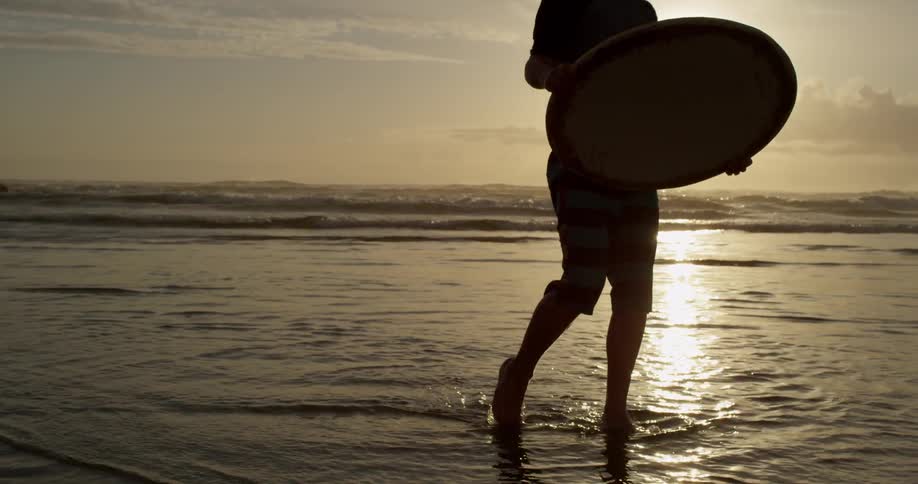 A boy walking along the water's edge, tossing a disk ski and running after it
