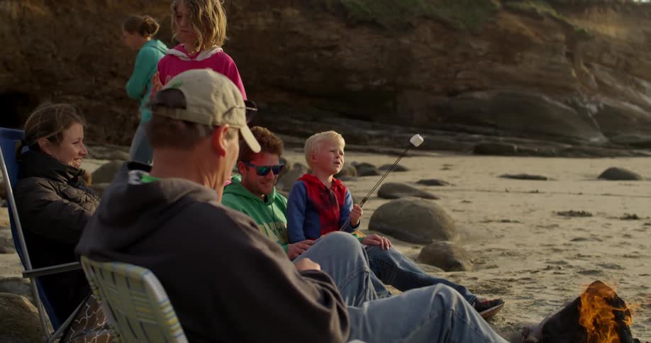 A family sits on the beach roasting marshmallows