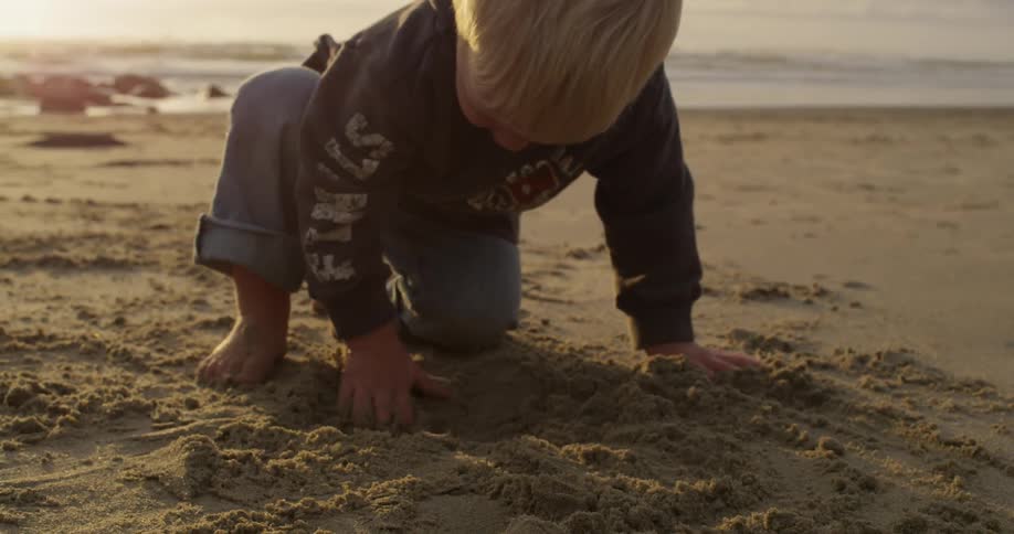 A boy plays with sand on a sunny beach