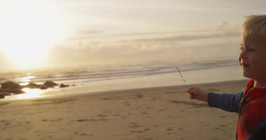 A little boy running along the beach with a sparkler in his hand