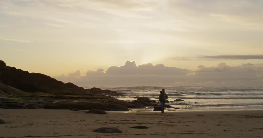 A man carries a child on a beach at sunset