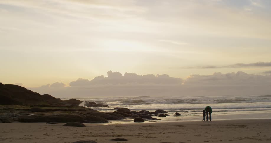 An adult and child are walking along the beach at sunrise
