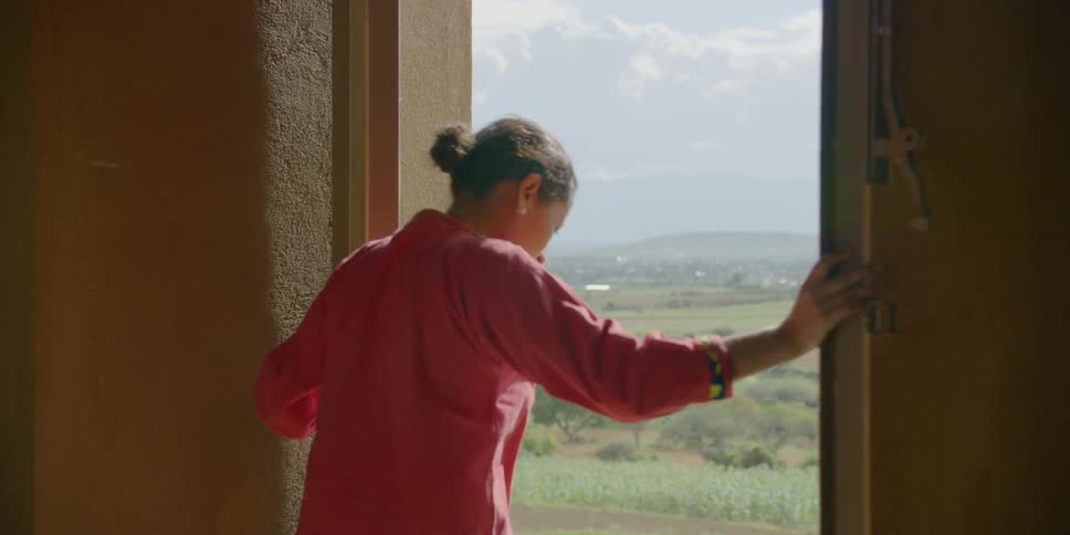 An hispanic woman opens up two large double doors and steps outside to look around