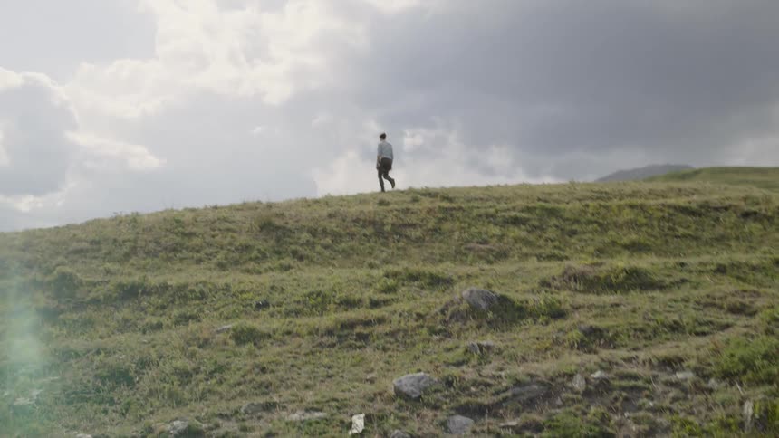Man walks up uneven slope to top of hill on cloudy day