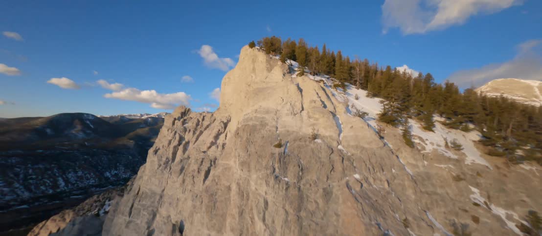 Trees and snow on a rocky ridge under a bright blue sky