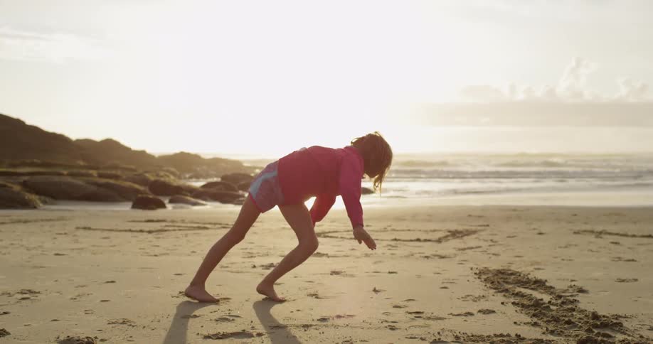 A girl does a cartwheel on the beach at sunset
