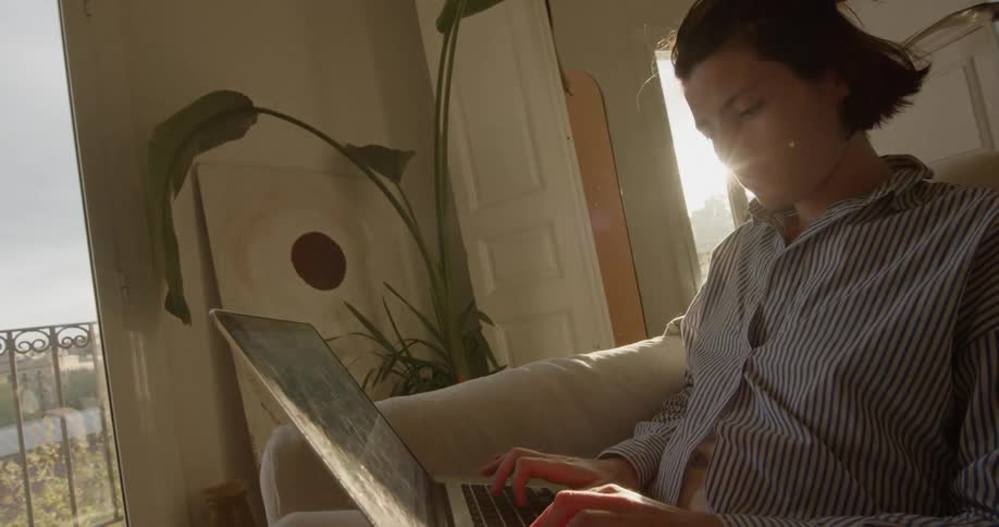 A male teenager sits and types on his laptop