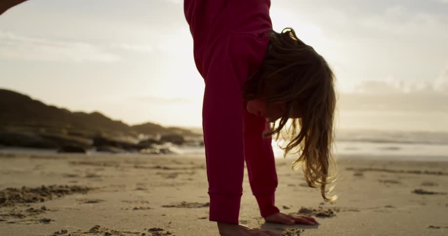 A girl stands on her hands in the sand on a beach