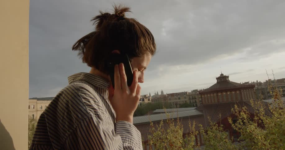 A woman speaking on a smartphone while standing on an outdoor balcony