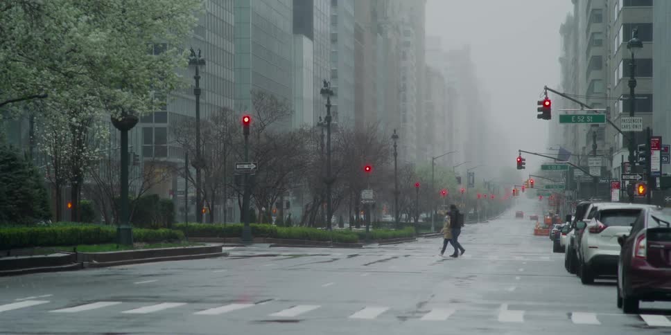 Pedestrians cross the city street as cars are parked nearby