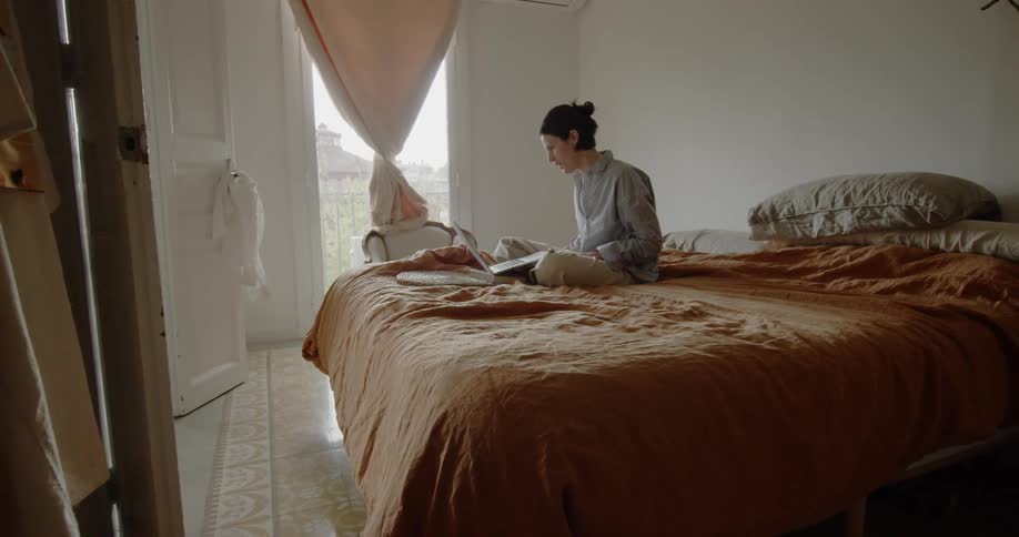 A person sitting on a bed looking at a laptop