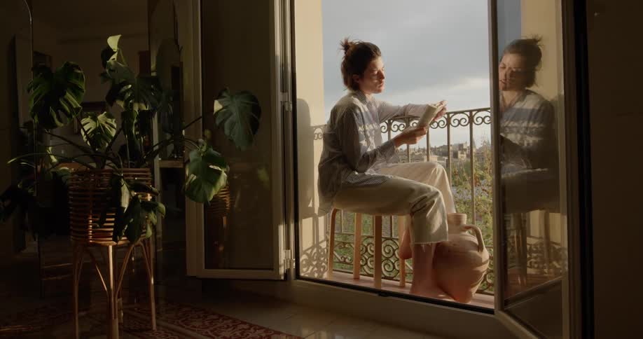 Man sitting on stool in the balcony of the apartment reads a book