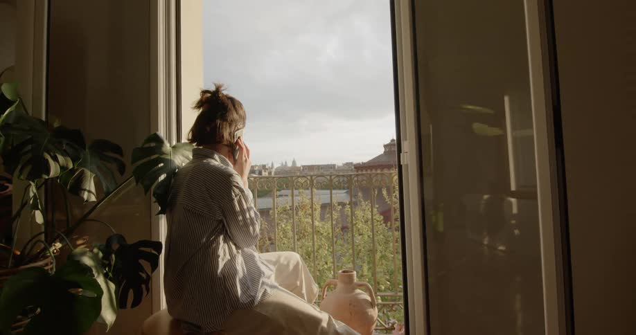 A woman sits in front of a balcony and talks on the phone