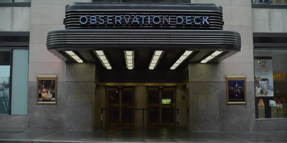 Display screen and signs are seen through windows of building with observation deck