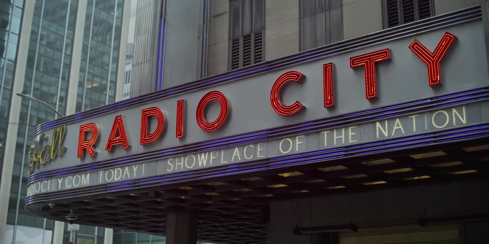 The lights of the radio city music hall marquee flicker and glow on a rainy day