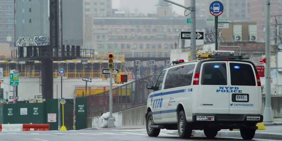 An nypd police van parked on an empty city street with back lights flashing blue and red