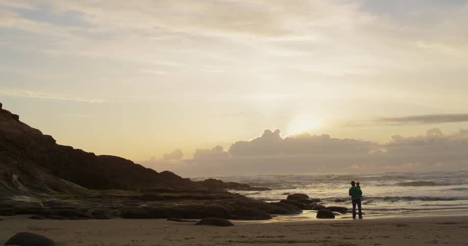 A man holds a young child on a beach at dusk