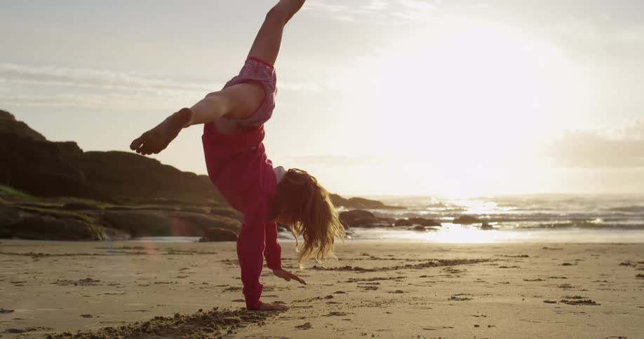 A girl does a cartwheel on the beach as the sun sets