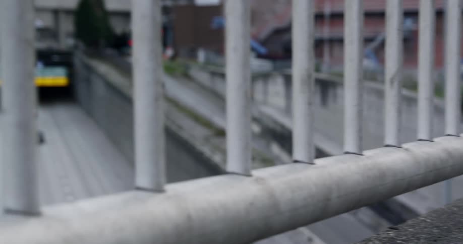 The railing on a sidewalk overlooks a multi lane highway with cars and trucks traveling in both directions