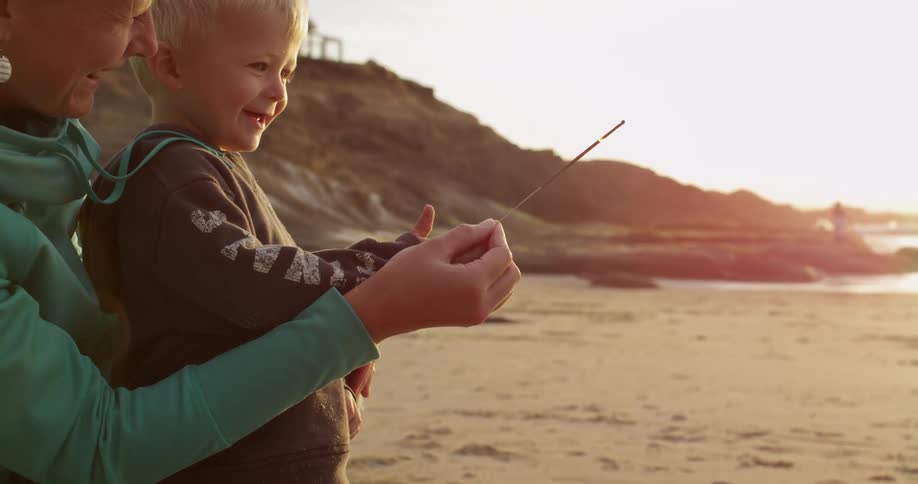 A boy and woman hold a burning sparkler on the beach