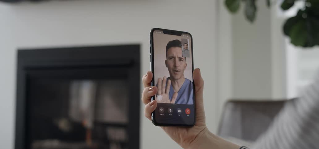 A phone screen shows a video call with a man in scrubs waving