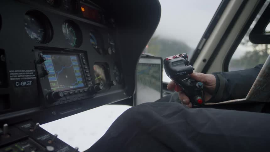 A pilot sitting in a helicopter cockpit grabs the control stick as he prepares for take off