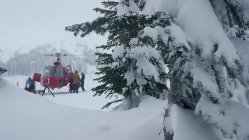 People cluster around helicopter on snow covered clearing in forest