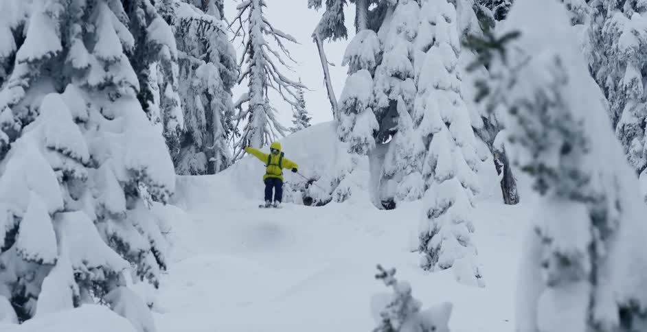 A person jumps off of a cliff while skiing down a mountain